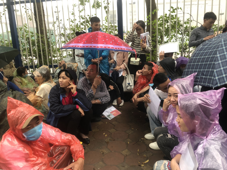 Người dân mặc áo mưa ngồi đợi mà không biết có được phát số hay không.